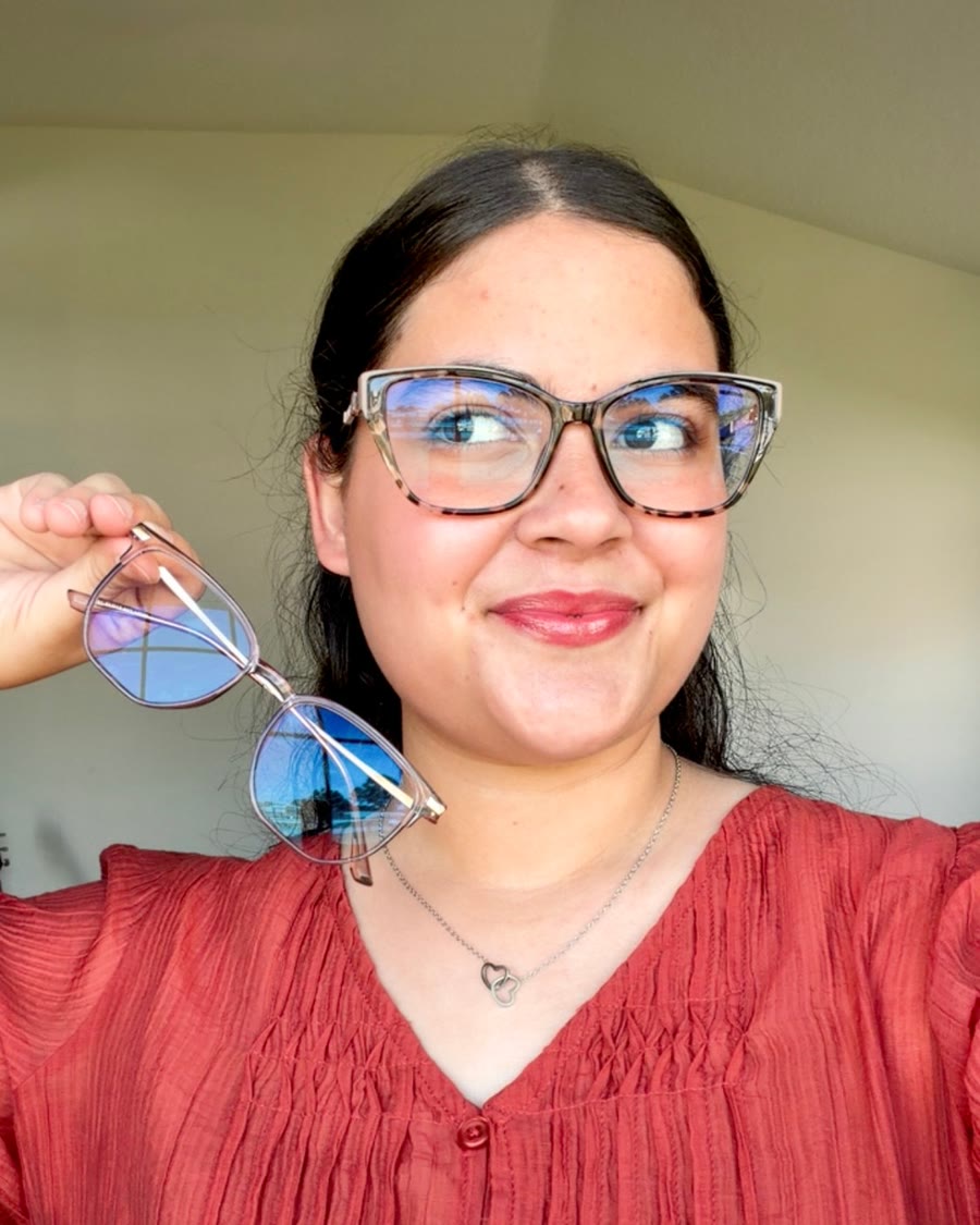 Kathlyn in glasses and a rust-colored blouse, smiling and holding up a second pair of glasses