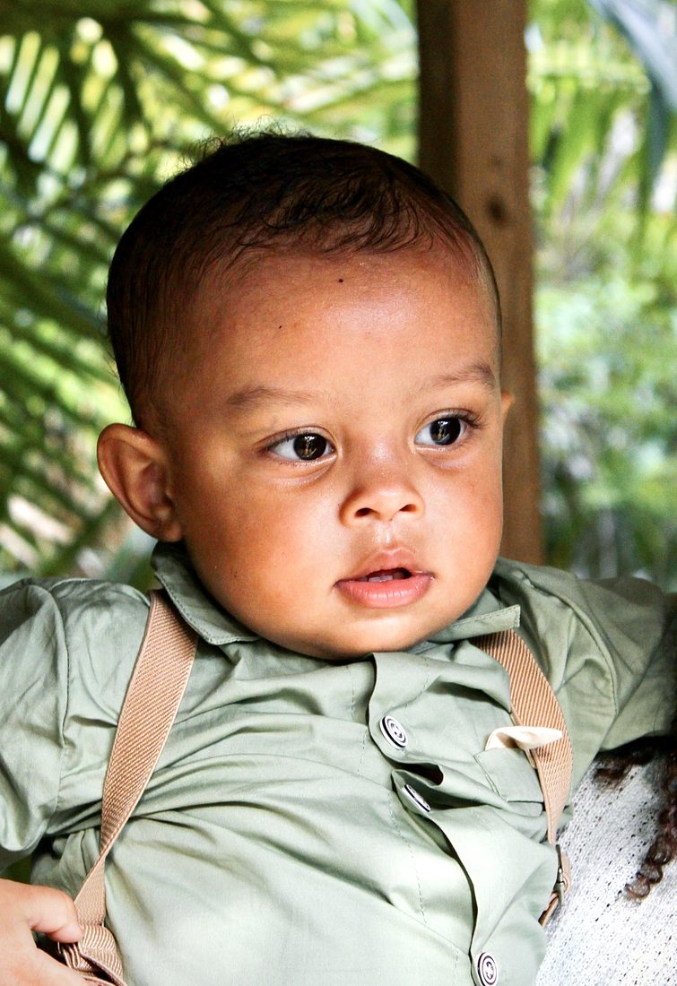 Close-up of a baby boy in a green outfit, looking off to the side