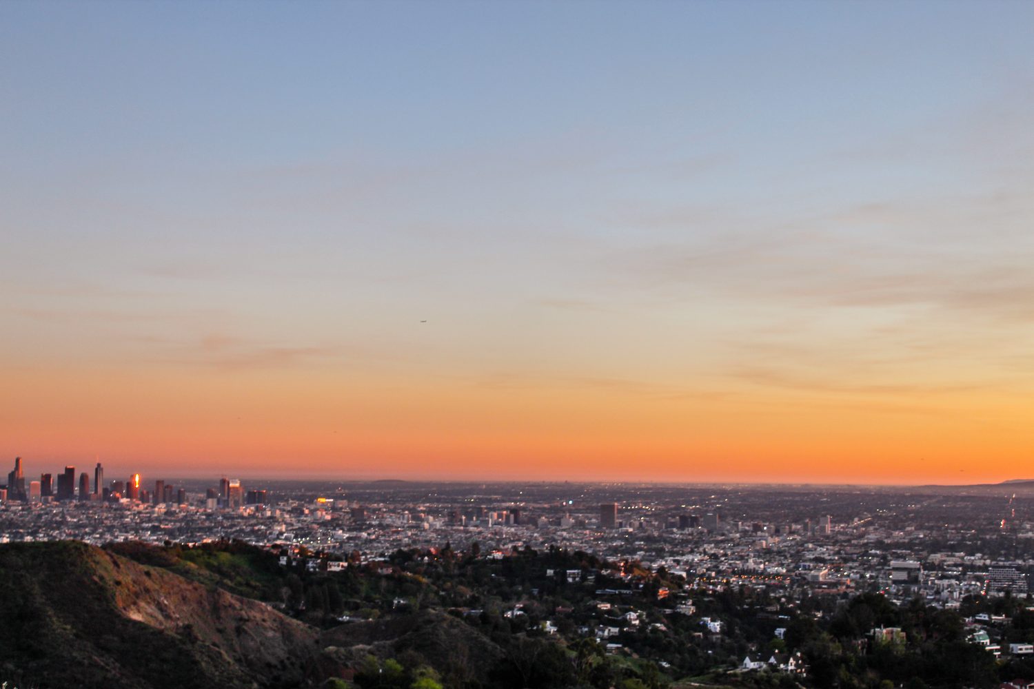 Orange and pink sunset over a city skyline seen from a hilltop