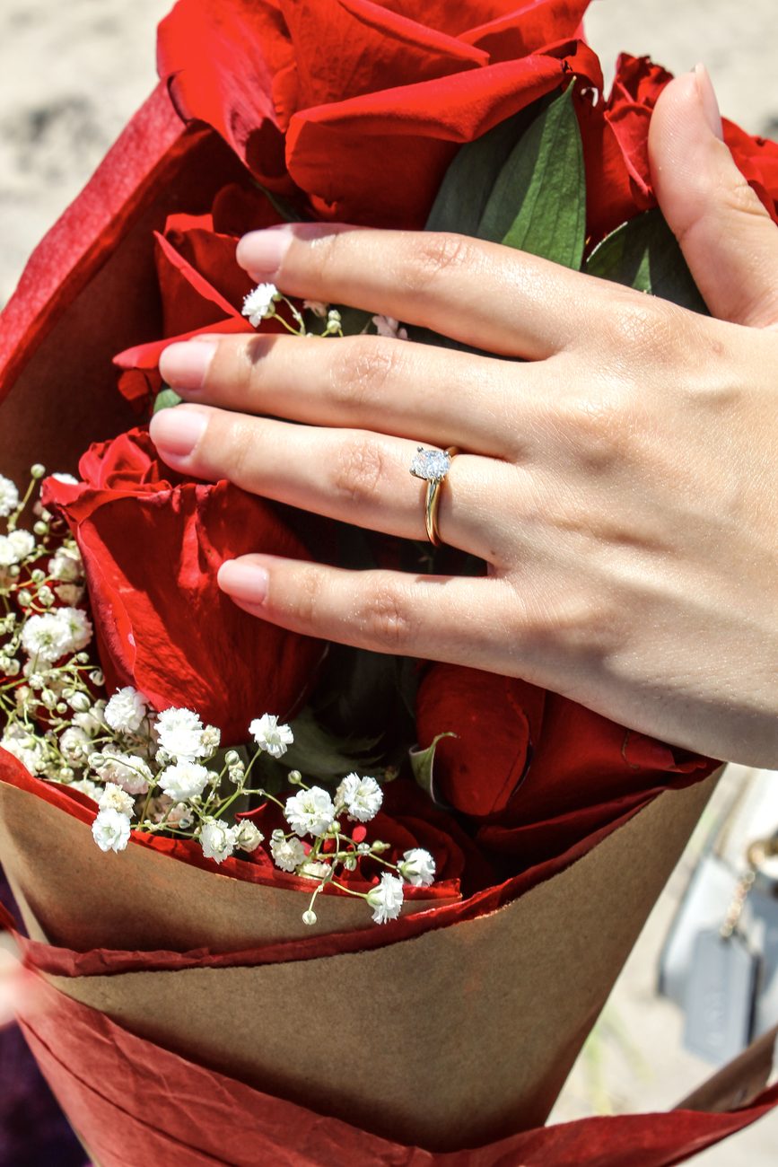 A hand wearing a diamond ring resting on a bouquet of red roses and baby's breath