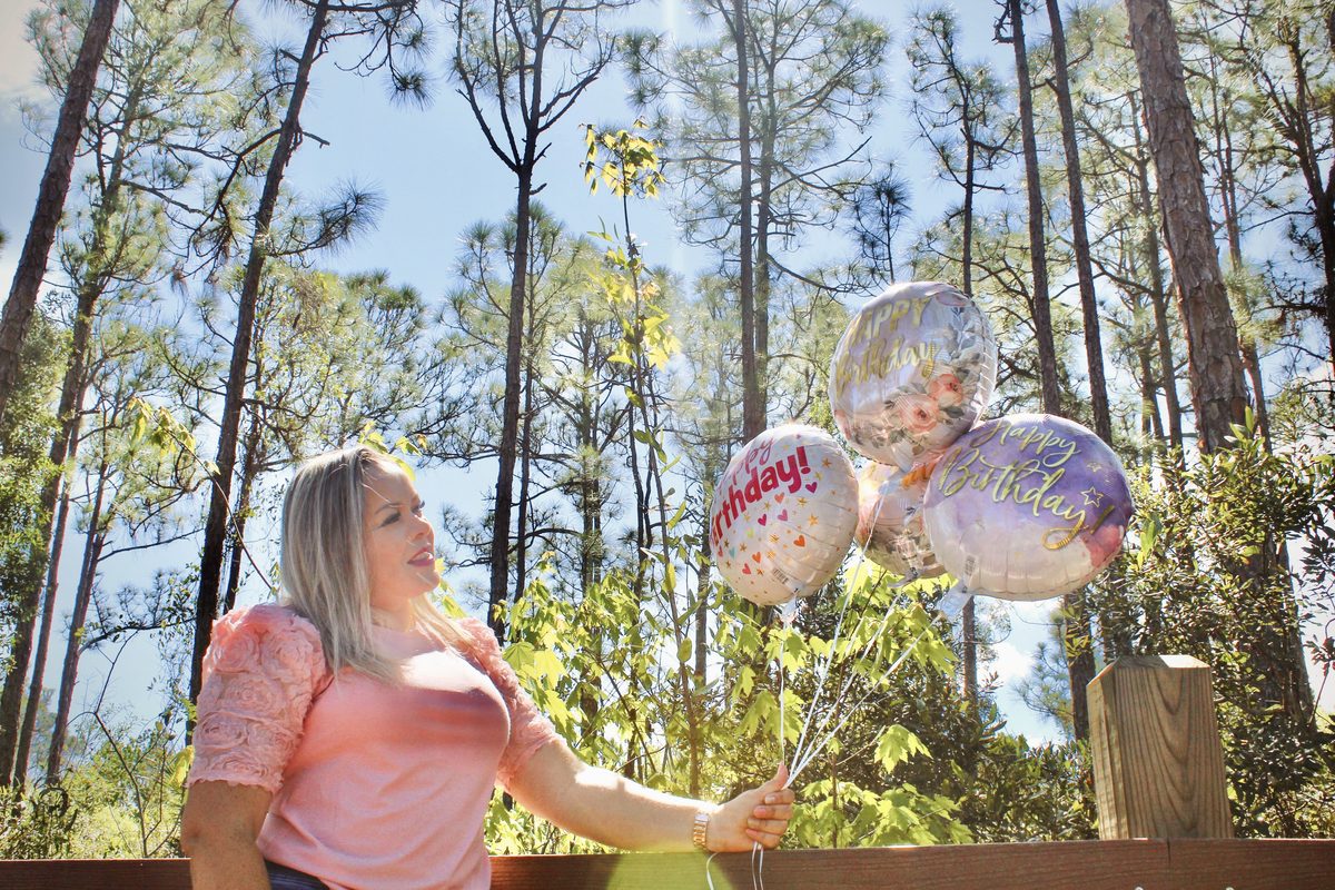 Woman in a pink top holding up a bunch of balloons on a wooden deck among tall pines
