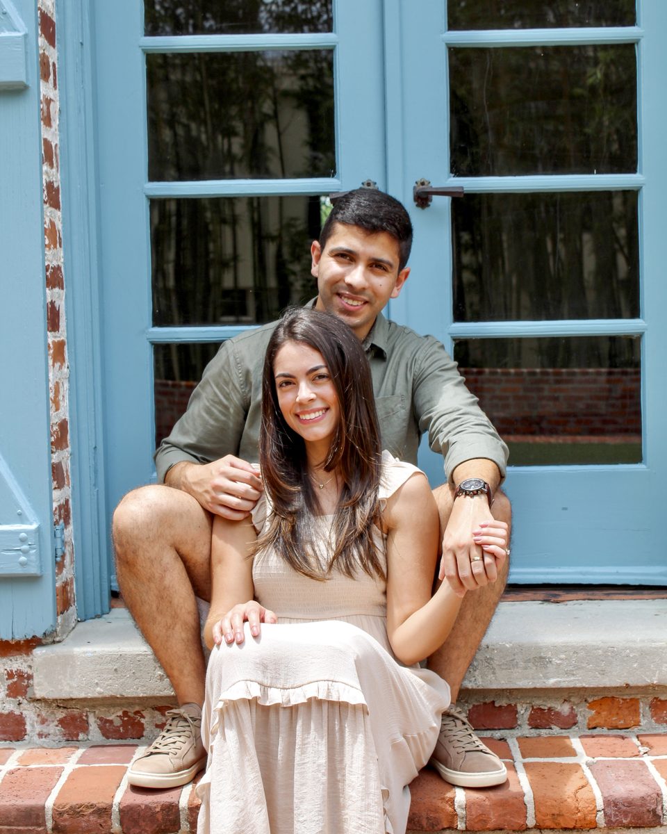 Couple sitting close together on brick steps in front of teal doors, smiling