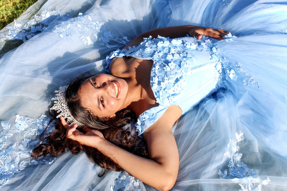 Girl in a light-blue gown and tiara lying back and smiling, the skirt spread around her