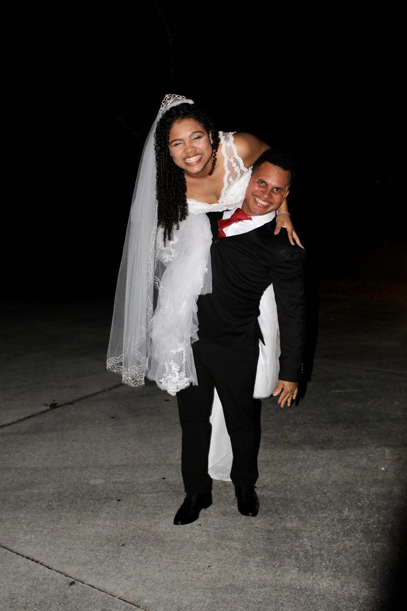Bride riding piggyback on her groom at night, both laughing, her veil trailing behind