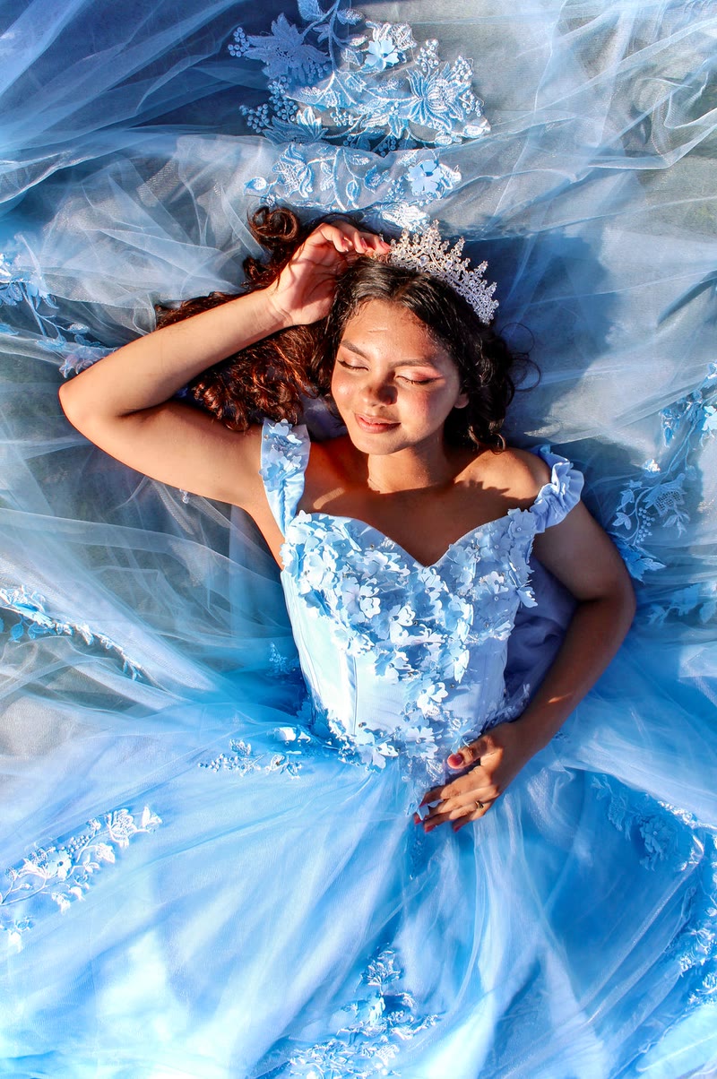 Girl in a sparkling light-blue gown and tiara, lying back with the skirt spread around her