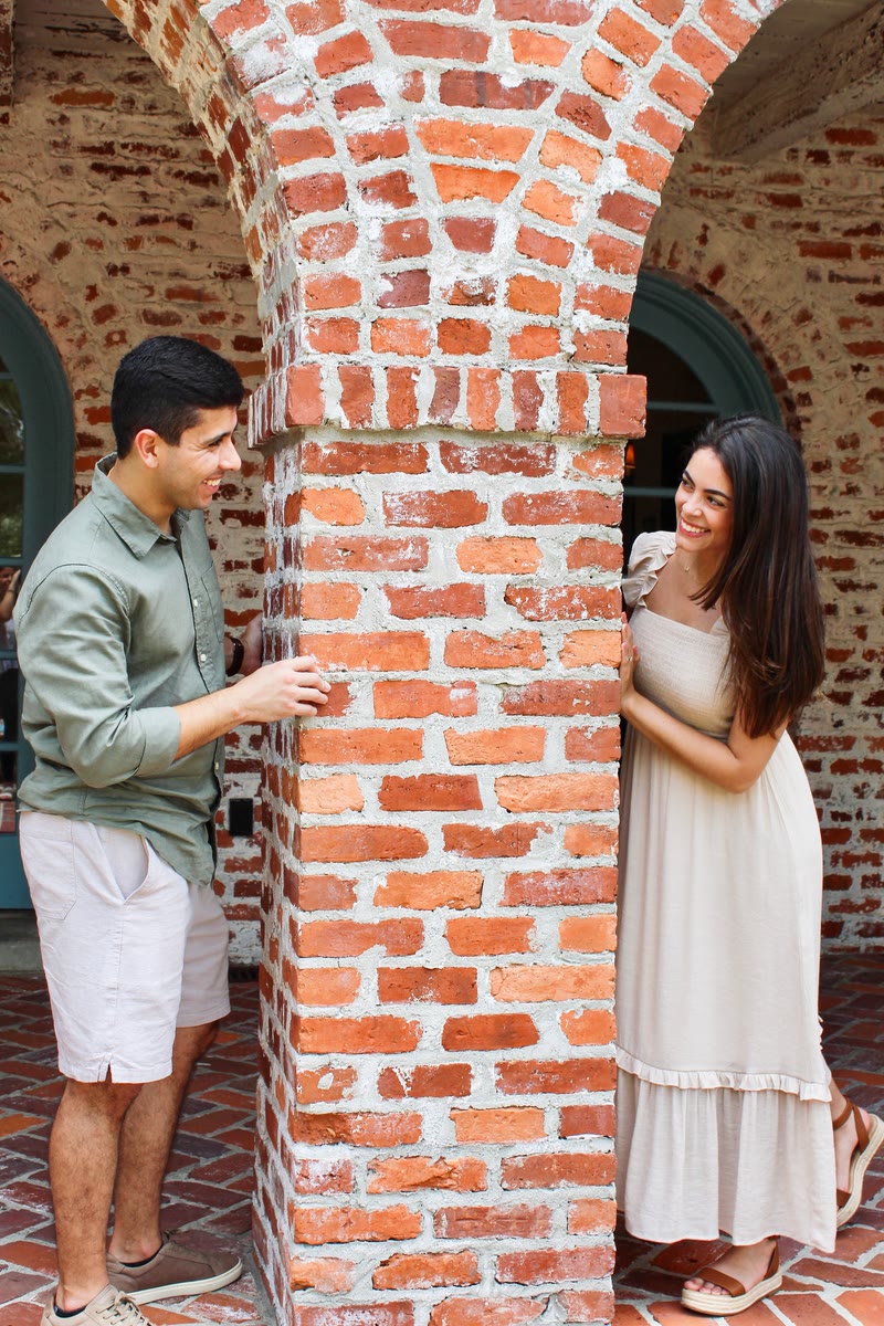 Couple smiling at each other from opposite sides of a red-brick archway pillar