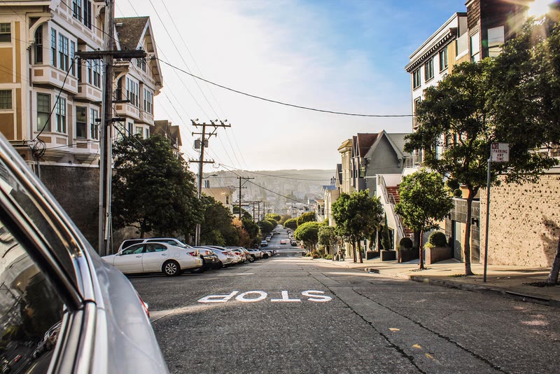 Sunny city street with parked cars, row houses and a hill in the distance