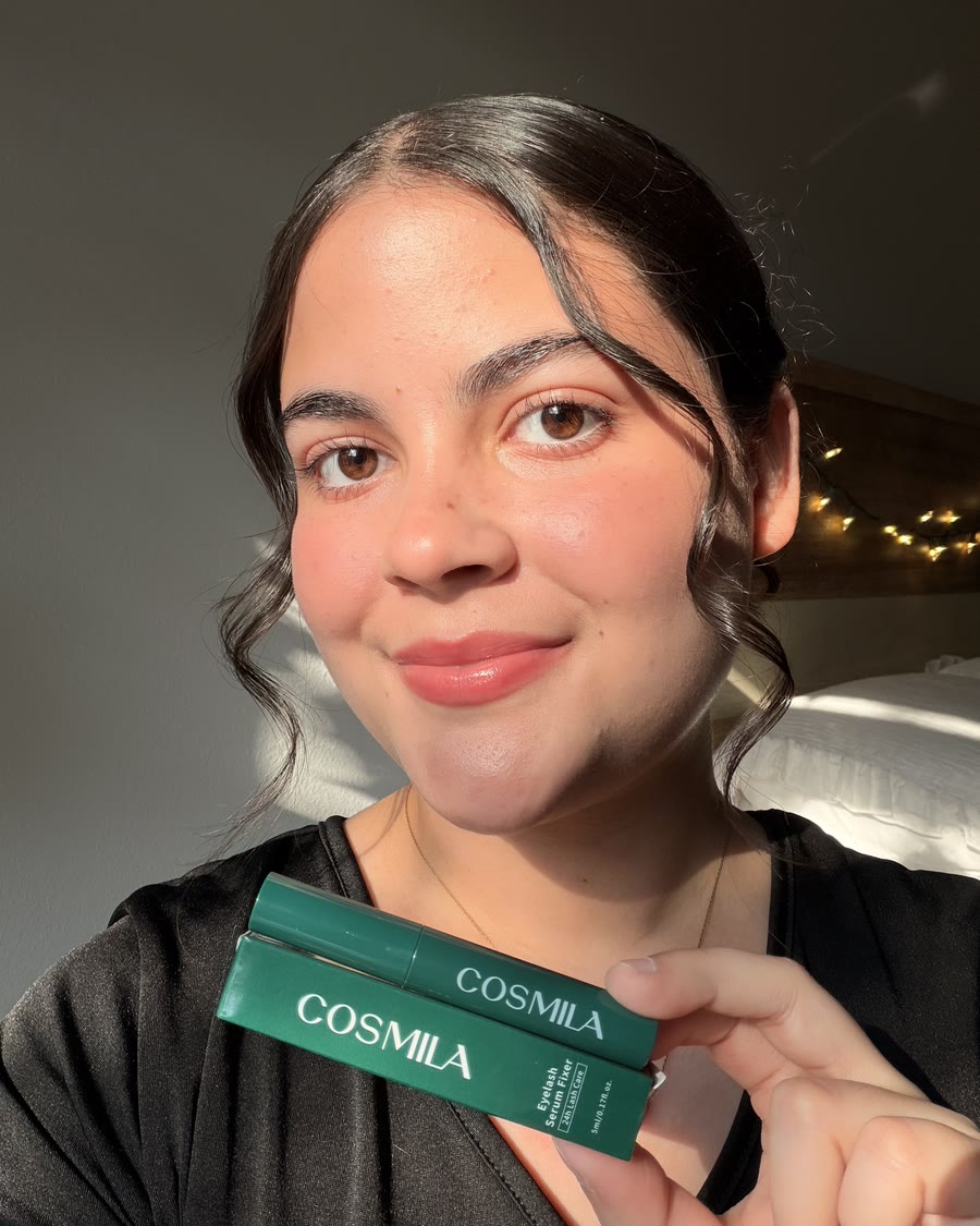 Kathlyn smiling in warm sunlight, holding up a green eyelash serum box