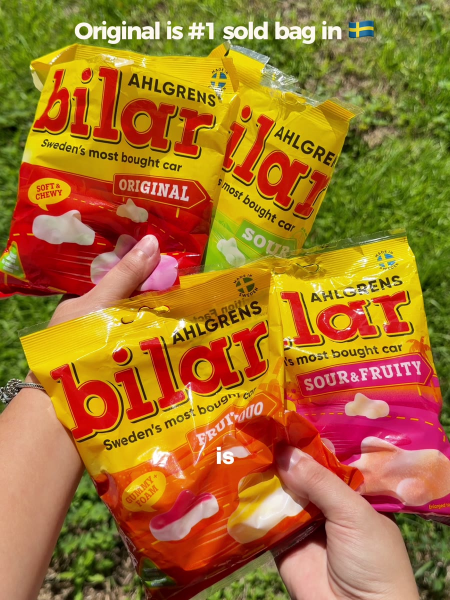 Four bags of Ahlgrens Bilar Swedish candy held up over grass: original, sour, sour and fruity, and fruity duo