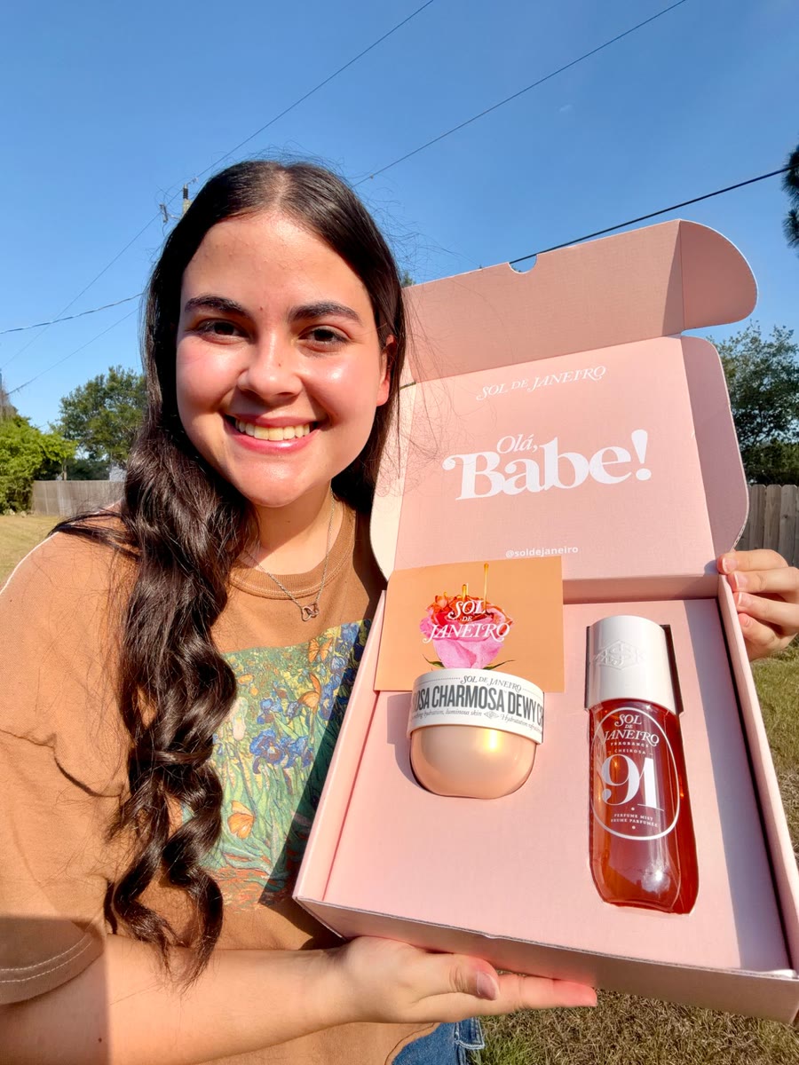 Kathlyn smiling in the sun and holding open a pink Sol de Janeiro PR box with a body cream and a fragrance mist inside